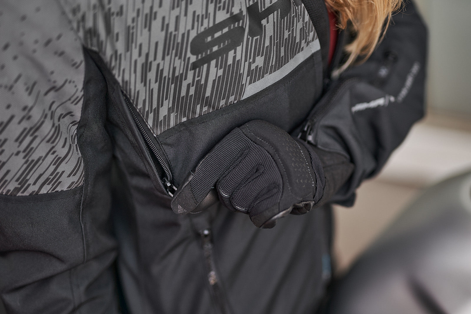 a hand unzipping the ventilation panel on the grey women&#39;s motorcycle jacket from SHIMA