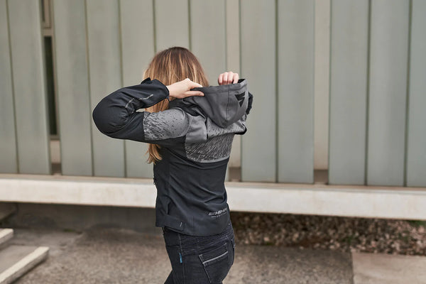 A woman is wearing a motorcycle grey jacket with a hood