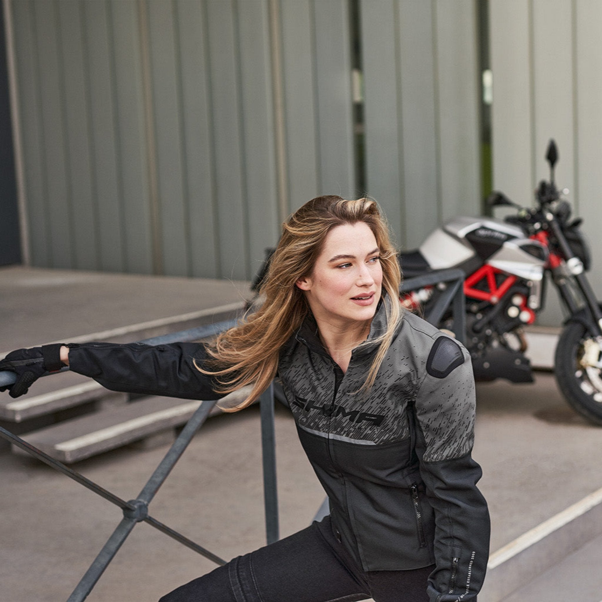 A blond woman near the motorcycle wearing grey women&#39;s motorcycle jacket from SHIMA