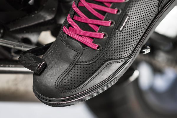 A foot wearing Rebel waterproof motorcycle sneakers with pink laces from Shima changing motorcycle gear