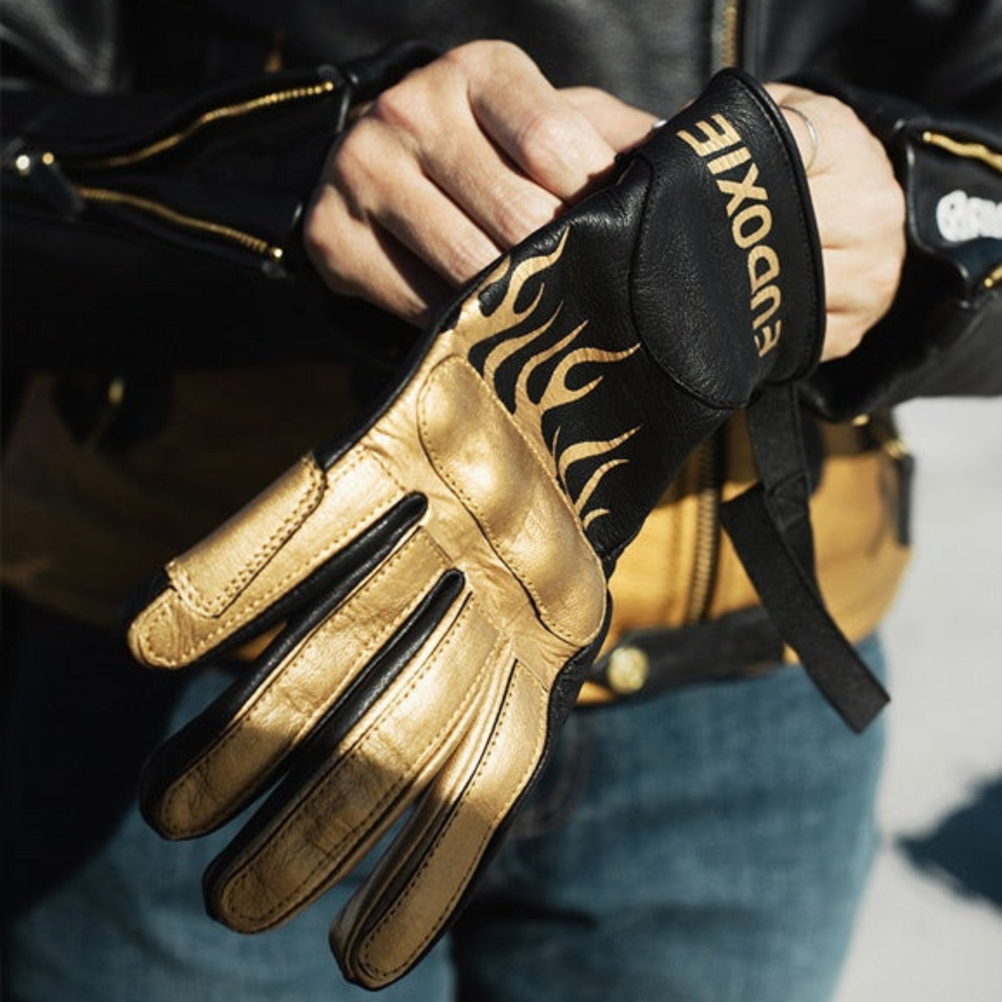 woman&#39;s hands putting on a black Eudoxie mc glove with golden flames 