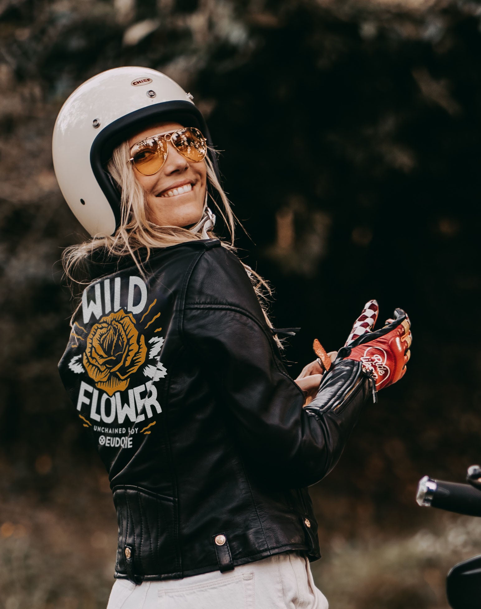 A smiling woman wearing motorcycle leather jacket for women from Eudoxie with the wild flower illustration on the back