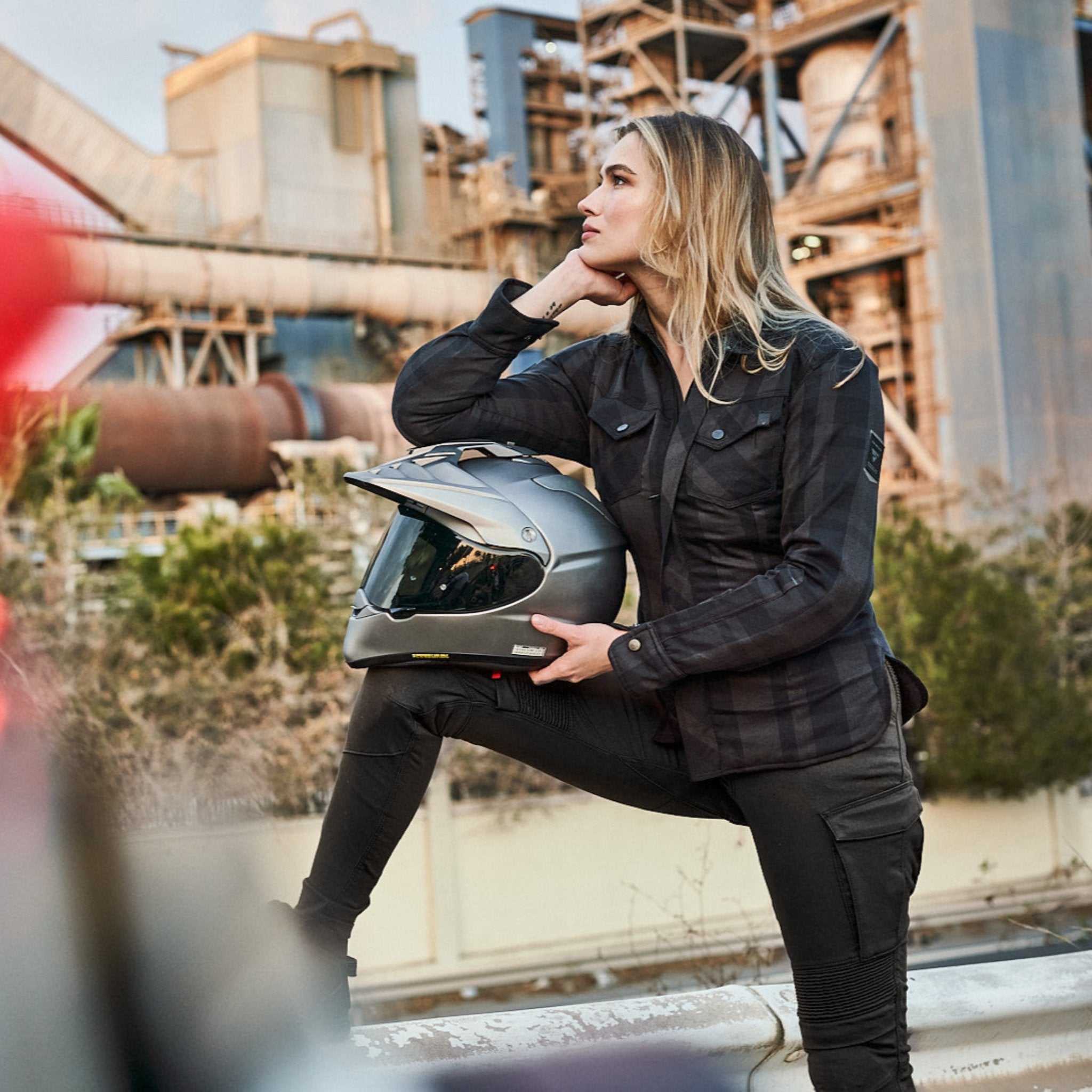 A young woman holding the helmet and wearing Khaki green women's motorcycle cargo pants GIRO from shima