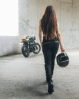En kvinde går hen imod sin motorcykel iført sorte damemotorcykeljeans