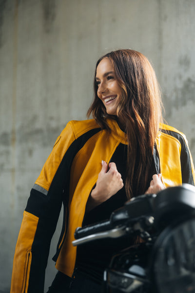 En ung kvinde på en motorcykel iført gul motorcykeljakke til damer