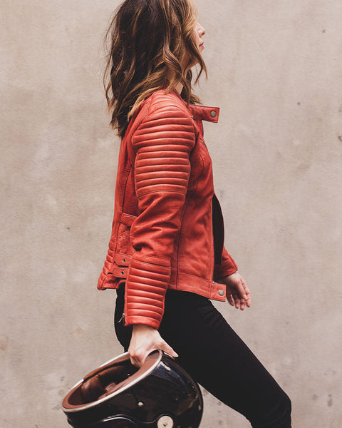 A woman carrying a helmet and wearing Women's red leather motorcycle jacket modern classic style from Black arrow label